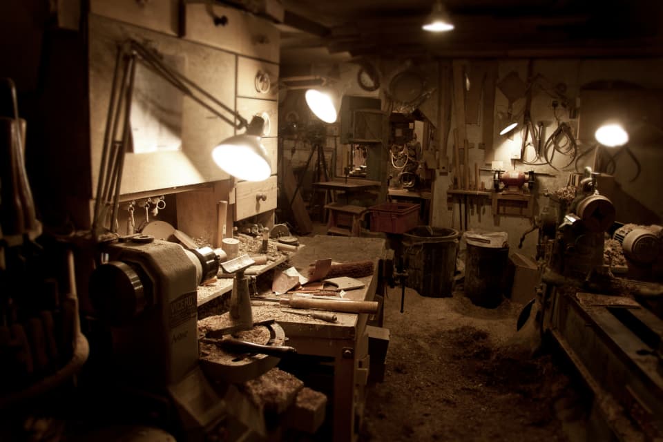 A carpenter's workshop under warm lamps: benches, a lathe, tools hung on the wall